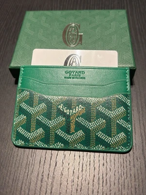 Grön korthållare  - Snygg grön korthållare från med det klassiska mönstret och loggan tryckt på framsidan. Tillverkad i exklusivt läder med flera fack för kort. Perfekt accessoar för dig som vill ha något både stilrent och unikt.