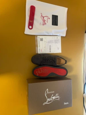 Christian Louboutin gråa sneakers - Snygga gråa sneakers från Christian Louboutin i mocka med klassisk röd sula. Låg modell med exklusiv känsla och ikonisk design. Perfekta för dig som vill sticka ut med stilrena detaljer och lyxig finish.