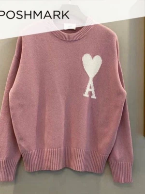 Rosa stickad tröja med hjärtdetalj - Trendig rosa stickad tröja med rund hals och ribbade muddar. På bröstet finns en vit hjärtdetalj med bokstaven 'A' under, vilket ger en unik look. Perfekt för dig som vill ha något gulligt och stilrent i garderoben. Oversized