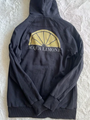  Acqua Limone hoodie - Svart hoodie från Acqua Limone med stor gul logga och text på ryggen samt mindre logga på bröstet. Klassisk känguruficka framtill, ribbade muddar och dragsko i huvan. Tillverkad i mjuk bomullsblandning, perfekt för en avslappnad stil.