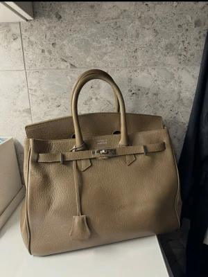 Olivgrön/brun handväska - Inte äkta men ska vara äkta läder, köpt utomlands för 2000 kr. Superfint skick endast använd någon enstaka gång. Varit nedpackad. Liten fläck på insida fodret (se nästsista bilden) annars inget 🤎olivgrön/brun, lite mer åt det bruna hållet i annan belysning. Kan såklart skicka fler bilder om så önskas!