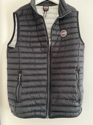 Colmar väst  - Snygg svart dunväst från Colmar med quiltad design och två dragkedjefickor framtill. Västen har hög krage, Colmar-logga på bröstet och är fodrad i ljusgrått. Perfekt för lager-på-lager och streetstyle. Barnstorlek 14y- motsvarar 166cm. Skriv för frågor/bilder, bara att kontakta!