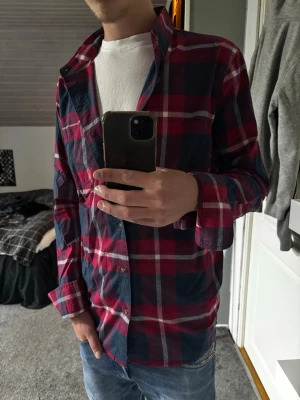Rutig Hollister skjorta - Säljer en röd och marinblå rutig skjorta från Hollister i storlek M. Skjortan har klassisk krage, knappar framtill och långa ärmar. Materialet är stretchigt och bekvämt, perfekt för en avslappnad stil.