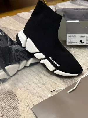 Balenciaga Speed Trainer svarta sneakers svart vitt - Svarta Balenciaga Speed Trainer sneakers med vit chunky sula och stickad strumpdesign. Skon har Balenciaga-logga på sidan och en elastisk ovandel i textil som sitter tight runt foten. Sulan är futuristisk och ger en sportig vibe.