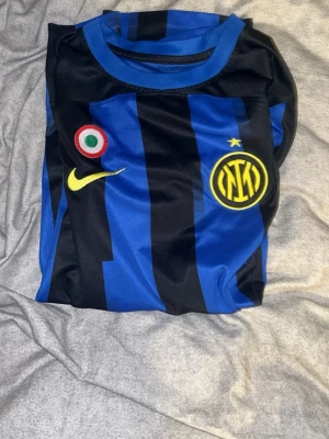 Inter Milan matchtröja blå/svart - Säljer en Inter Milan matchtröja från Nike i blått och svart med klassiska vertikala ränder. Tröjan har klubbmärke och Nike-logga på bröstet samt en gul stjärna ovanför klubbmärket. Tillverkad i lätt och ventilerande material, perfekt för fotboll eller träning. Ingen på ryggen 