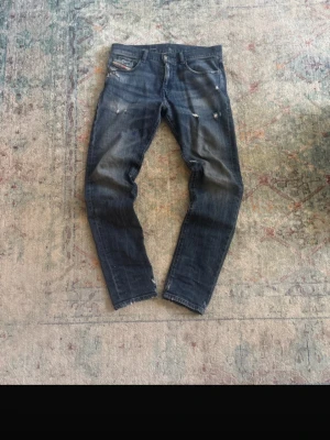 Mörkblå slitna jeans från Diesel - Säljer ett par mörkblå jeans från Diesel med slitningar och distressed detaljer. Klassisk femficksmodell med normal passform och snygg tvätt. Perfekta för en avslappnad och trendig look.