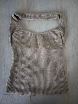 Guldig ribbad stickad linnetopp - Säljer en guldig ribbad stickad linnetopp med breda axelband och figurnära passform. Toppen har en enkel och stilren design. Materialet är mjukt och stretchigt. 