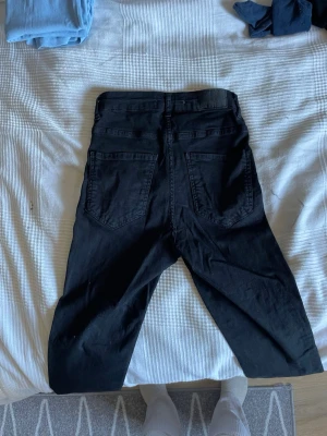 Svarta skinny jeans från Gina Tricot - Säljer ett par svarta skinny jeans från Gina Tricot med hög midja och klassiska fem fickor. Jeansen har dragkedja och knapp framtill samt smal passform hela vägen ner. Perfekta till en avslappnad eller trendig look.