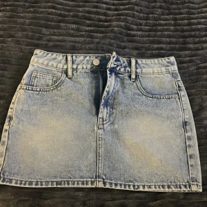 Ljusblå jeanskjol med fickor -  ljusblå jeanskjol i kort modell med femficksdesign och bälteshällor. Kjolen har en lätt tvättad look och stängs med knapp och dragkedja framtil.