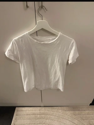 Vit  t-shirt från 157 - Vit t-shirt från 157 i 100% bomull. T-shirten har korta ärmar och rund halsringning, perfekt till jeans eller kjol för en clean och avslappnad look.