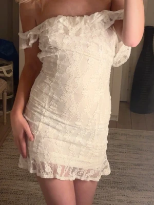 Vit spetsklänning offshoulder - Säljer en vit kortklänning med offshoulder-design och volangdetaljer. Klänningen är gjord i spetsmaterial och har en feminin, figurnära passform. Perfekt för dig som vill ha en romantisk look med snygga detaljer.