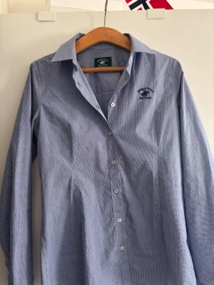 Blårutig skjorta från U.S. Polo Assn. - Klassisk blårutig skjorta från U.S. Polo Assn. med diskret logga broderad på bröstet. Skjortan har lång ärm, knappar framtill och en snygg krage. Tillverkad i bomull för en skön känsla och perfekt passform.