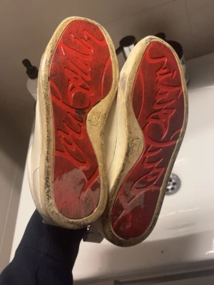Vita sneakers från Christian Louboutin - Säljer ett par vita sneakers från Christian Louboutin med klassiska röda sulor och vita skosnören. Skorna har en stilren design i läder och den ikoniska loggan under sulan. Dem är i lite sämre skick därav priset. OBS BOX OCH KVITTO INGÅR