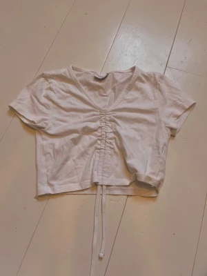 Vit croppad topp från Noisy May - Säljer en vit croppad topp från Noisy May med v-ringning och snörning framtill. Toppen har korta ärmar och är gjord i mjuk bomull, perfekt för en avslappnad och trendig look.