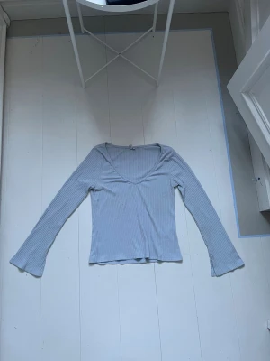 Ljusblå ribbad långärmad topp - Ljusblå långärmad topp med v-ringning och ribbad struktur. Ärmarna har en liten slitsdetalj vid ärmsluten som ger en extra touch. Perfekt att styla med jeans eller kjol för en chill look.