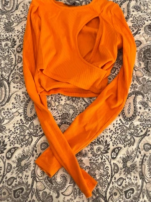 Orange ribbad topp  - Trendig orange långärmad topp från Sister i ribbad bomullsmix. . Perfekt för dig som vill sticka ut med färg och coola detaljer.