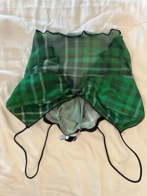 Grön rutig mesh linnetopp - Trendig grön linnetopp i mesh med rutigt mönster och tunna svarta axelband. Toppen har en croppad passform och vågig kant nedtill. Perfekt för att skapa en cool och ungdomlig look. Helt oanvänd
