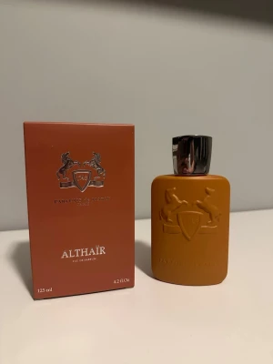 Parfums de Marly Althaïr EdP - Exklusiv parfym från Parfums de Marly, Althaïr Eau de Parfum i en snygg matt orange flaska med silverfärgat lock. Flaskan har ett elegant reliefmönster med två hästar och sköld. Kommer i matchande orange kartong. Volym: 125 ml.