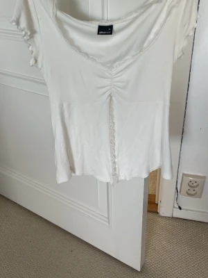 Vit topp med spetsdetaljer  - Söt vit topp från Gina Tricot med korta ärmar, v-ringning och fina spetsdetaljer längs halsringningen och framtill. Pris kan diskuteras och skicka om ni har frågor! Storlek XS. 
