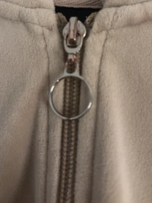 Beige hoodie med dragkedja - Säljer en beige hoodie med dragkedja och rund metallring som dragkedje-dragare. Hoodien är gjord i mjukt tyg och har en enkel, stilren design. Perfekt för dig som gillar en clean och avslappnad look.