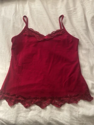 Vinröd linnetopp med spetsdetaljer - Snygg vinröd linnetopp med tunna axelband och spetsdetaljer vid halsringning och nederkant. Perfekt för lager på lager eller som statement-plagg. Mjuk och skön känsla.