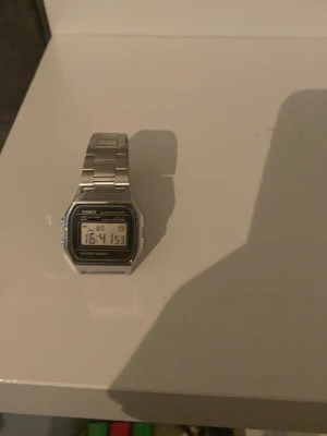 Casio digital klocka i silver - Klassisk digital klocka från Casio med rektangulär display och armband i silverfärgad metall. Klockan har tydlig digital tidvisning, datum och veckodag på displayen. Perfekt för dig som gillar retrostil och enkel design.