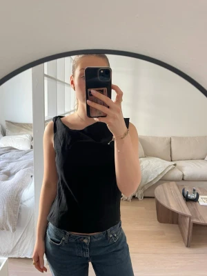 Svart linnetopp - Snygg svart linnetopp med bredare axelband och en sidan är tvistad. Toppen har en clean och stilren look som passar till både vardags och fest.  Aldrig använd och prislapp kvar!