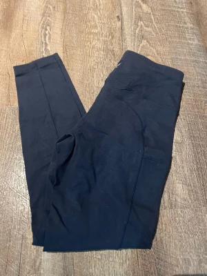 Svarta tights med ficka - Säljer ett par svarta tights perfekta för träning eller gymmet. De har en smidig ficka på sidan för mobilen och är sydda i ett stretchigt material som sitter skönt mot kroppen. Snygg sömdetalj längs benen för extra stilpoäng.