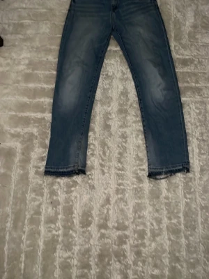 Blå flared jeans  - Säljer ett par blå jeans med flared  passform och rå, fransad kant nedtill. Jeansen har klassisk femficksdesign och ljusa slitningar på låren och knäna för en avslappnad look. Perfekta för dig som gillar en trendig och casual stil.
