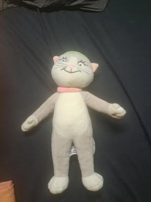 Pelle Svanslös katten - Söt mjukisdocka i form av en katt med ljusgrå kropp, vit mage och tassar, rosa halsduk och öron samt en grön keps med blå detalj. Katten har broderat ansikte och svans. Perfekt som gosedjur eller dekoration.