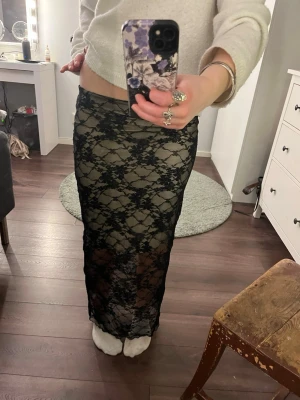 Svart långkjol i spets - Säljer en svart långkjol i transparent spets med blommigt mönster. Kjolen har en figurnära passform och är perfekt för dig som vill ha en trendig och edgy look. Materialet är mjukt och följsamt, vilket gör den bekväm att bära.