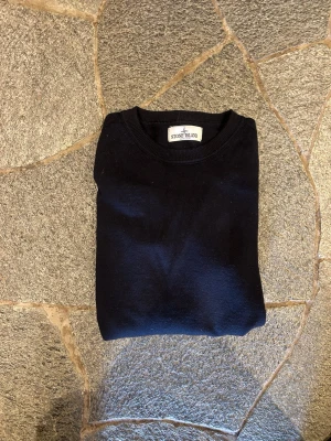 Mörkblå stickad tröja Stone Island - Snygg mörkblå stickad tröja från Stone Island med klassisk rund hals och ikonisk logotyp-patch på ärmen. Tröjan har en enkel och stilren design som passar perfekt till många olika outfits. Materialet är mjukt och bekvämt. Nypris runt 3449, mitt pris: 449