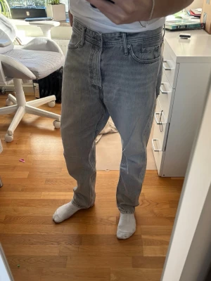 Grå jeans JACK AND JONES - Säljer ett par gråa raka jeans från  JACK AND JONES  med klassisk femficksdesign och hög midja. Jeansen har en avslappnad passform och är tillverkade i slitstark denim. Perfekta för en casual och trendig look.