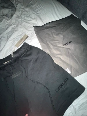 Essentials Fear of God Svarta shorts - Svarta shorts från Essentials Fear of God med dragsko i midjan och logga framtill. Sköna och stilrena, perfekta för en chill och trendig look. Kommer med originalpåse och tag kvar.