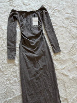 Grå långklänning från Bershka - Snygg grå långklänning från Bershka med offshoulder-design och långa ärmar. Klänningen har en figurnära passform och är tillverkad i mjukt material. Aldrig använd med prislappen kvar, storlek XS.