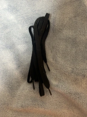 Svarta skosnören i textil - Ett par klassiska svarta skosnören i textilmaterial. Perfekta för sneakers eller boots, med platta ändar och en stilren look. Passar till de flesta skor och ger en clean vibe till outfiten.
