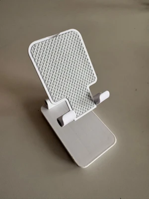 Vikbart vitt mobilställ - Snyggt och praktiskt vikbart mobilställ i vit plast med grått mönstrat stöd. Perfekt för att hålla mobilen på plats när du kollar på videos eller pluggar. Passar de flesta smartphones och är lätt att ta med sig tack vare den kompakta designen.
