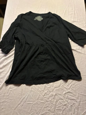 Svart omlottblus med trekvartsärm - Stilren svart omlottblus från Soul River med djup V-ringning och trekvartsärmar. Blusen har en avslappnad passform och är tillverkad i ett mjukt, lätt material som känns skönt mot huden. Perfekt att matcha med jeans eller kjol för en trendig look.