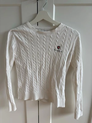 Vit kabelstickad tröja - Kabelstickad tröja i vitt från Bondelid med rund hals och broderad logga på bröstet. Långa ärmar och ribbade muddar vid ärmslut och nederkant. Klassisk och stilren modell i mjukt material.