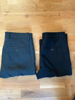 Zara Melagne Byxor - 2 par!! Strl. 38 - Två par klassiska kostymbyxor i svart och mörkgrå färg. Byxorna har raka ben, bälteshällor och bakfickor med knapp. Perfekta för en stilren look och passar till skjorta eller t-shirt. Materialet är  en mjuk bomullsblandning.