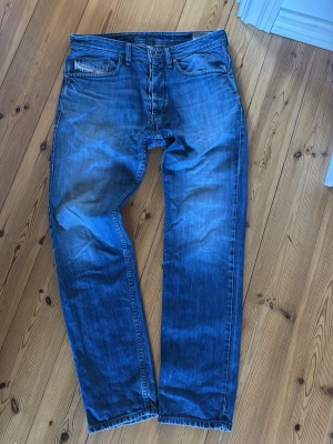 Blå raka jeans från diesel - Säljer ett par klassiska blå jeans från diesel med rak passform och sitter med lite bootcut. Jeansen har snygga slitningar och kontrastsömmar, samt en liten logotyp på myntfickan.