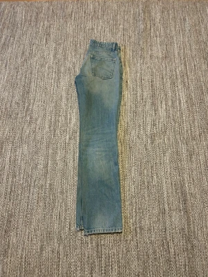 Blå raka jeans med vintagekänsla - Säljer ett par klassiska blå jeans med rak passform och lätt tvättad look. Jeansen har fem fickor och normal midja. Perfekta för dig som gillar en avslappnad och tidlös stil. Jeansen stängs med knappar