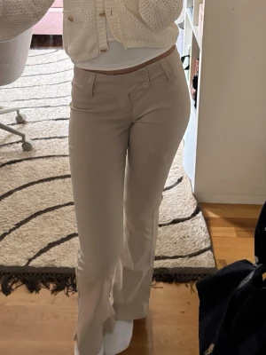Beige bootcut byxor med dubbelknapp - Säljer ett par snygga beige bootcut byxor med dubbelknapp framtill. Byxorna har låg midja och är tillverkade i ett mjukt bomullsmaterial. Perfekta för dig som gillar en stilren och trendig look.