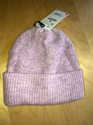 Ljuslila stickad mössa från Zara - Säljer en ljuslila stickad mössa från Zara med bred uppvikt kant och diskret hålmönster. Mössan är mjuk och har en klassisk form som passar perfekt till kalla dagar. Materialet ser ut att vara en ullblandning för extra värme och komfort.