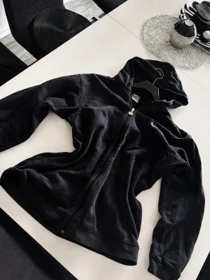 Svart zip hoodie från Nike - Säljer en svart hoodie från Nike med dragkedja framtill och två fickor. Hoodien har en liten Nike-logga på bröstet och är tillverkad i mjukt material. Perfekt för en avslappnad och sportig stil. Inga skador men man ser tydligt hoddie är advänd den ser inte ny ut.
