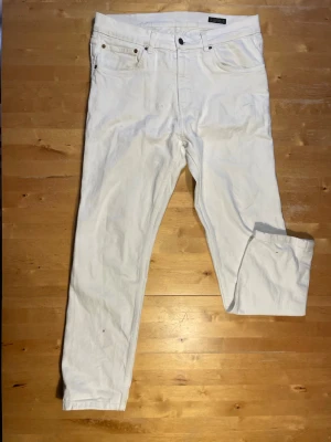 Vita raka jeans  - Säljer ett par vita jeans med rak passform och klassisk femficksdesign. Jeansen har normal midja och är tillverkade i ett kraftigt bomullstyg. Perfekta för dig som vill ha en clean och stilren look.