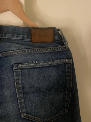 Ralh lauren Jeans  - Säljer ett par klassiska blå jeans från ralh lauren med smal passform och snygga slitningar. Jeansen har fem fickor, läderpatch bak i midjan och coola sömdetaljer på bakfickan. Perfekta till en avslappnad stil och tillverkade i mjukt denimtyg.