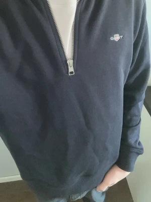 Marinblå half-zip tröja från Gant - Snygg marinblå tröja från Gant med halv dragkedja och diskret logga på bröstet. Tröjan har långa ärmar, ribbade muddar och är tillverkad i mjukt material som passar perfekt till jeans eller chinos.
