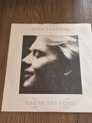 John Farnham singel You're The Voice - Vinylsingel med John Farnham, låten 'You're The Voice' och B-sidan 'Going, Going, Gone'. Omslaget är vitt med svartvitt foto och tryckt text. Skivan är utgiven av RCA och har detaljer om produktionen på baksidan.