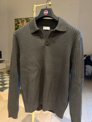 Stickad tröja från These Glory Days - Snygg mörkgrön stickad tröja från These Glory Days med ribbad struktur och krage. Tröjan har knäppning vid halsen och långa ärmar. Perfekt för dig som gillar stilrena och klassiska plagg i garderoben. Endast använd en gång.